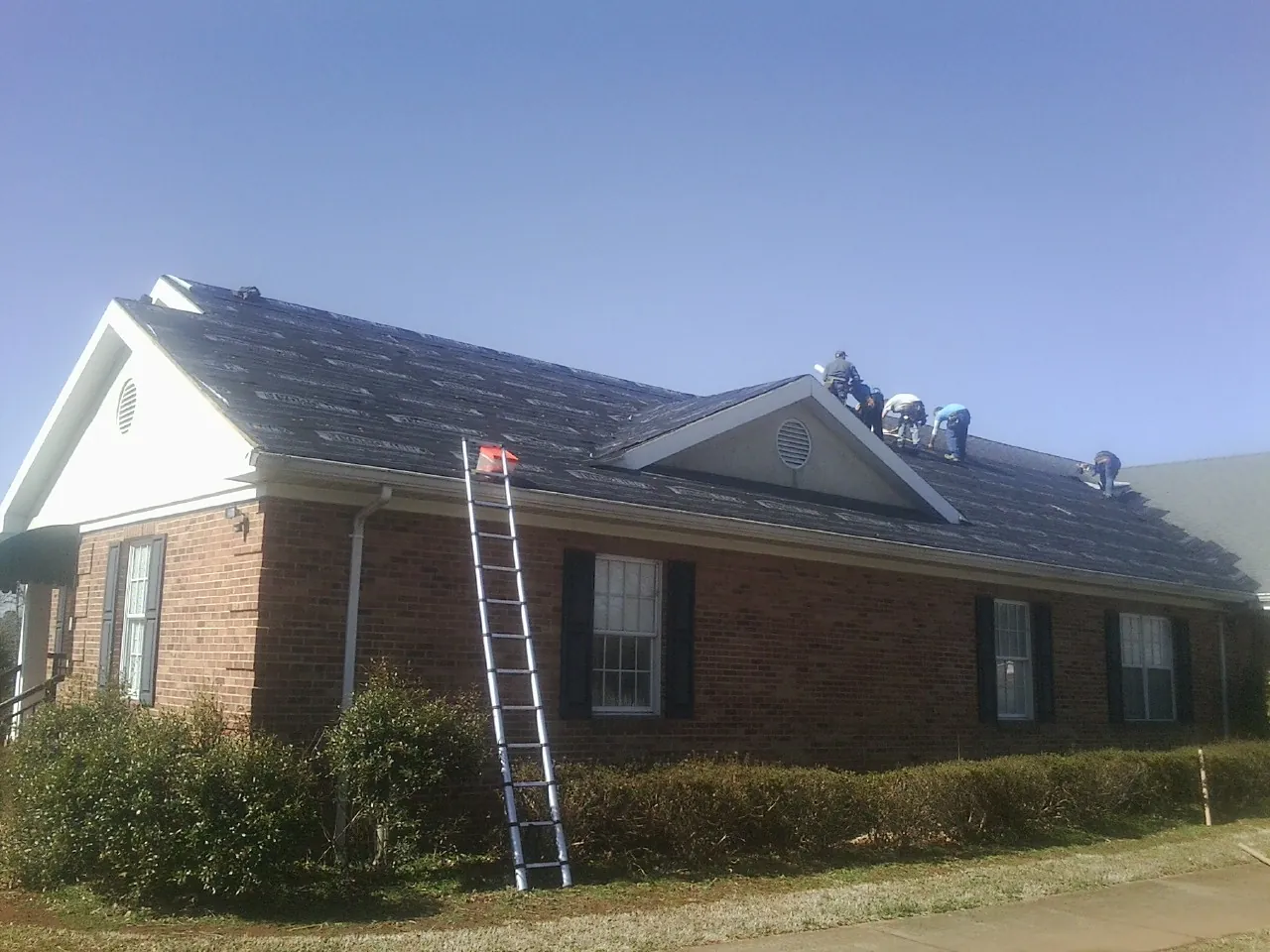 Crew tearing shingles off a brick ranch roof with a ladder set — Emergency Roof Repair work by our crew in Gibson Island