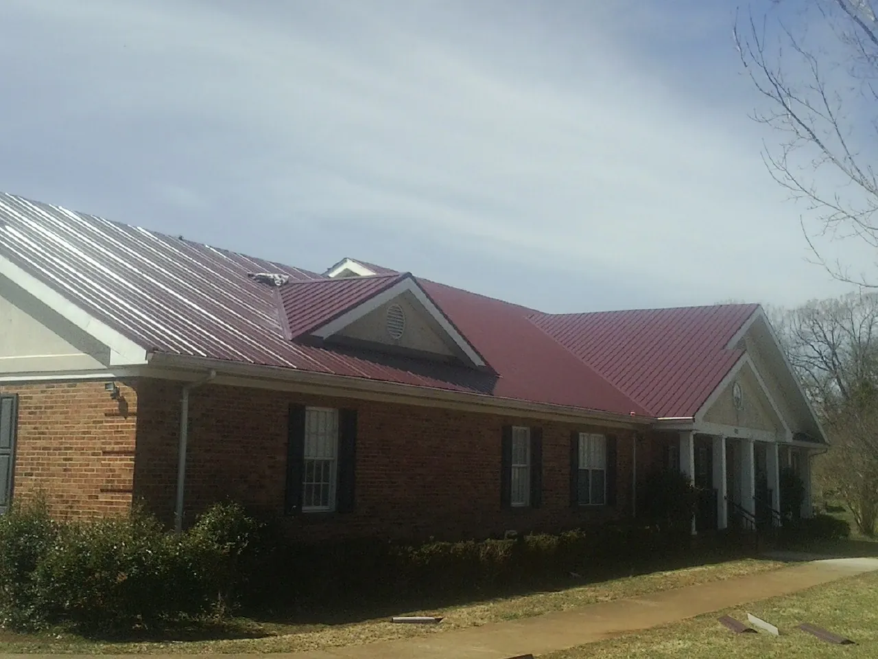 Red metal roof with gabled entries on a long brick building, from a Hail Damage Roof Repair job in Gibson Island