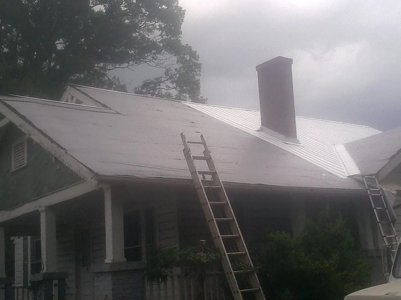 Ladders against a metal roof on an older home with a brick chimney in Gibson Island