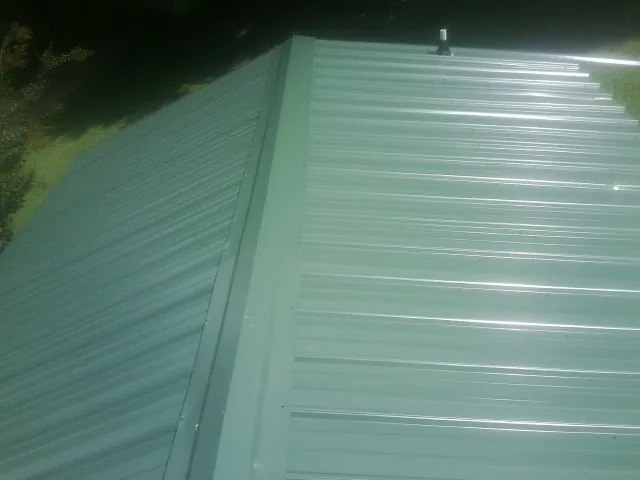New green metal panels meeting at the ridge of a roof — Flat Roof Repair work by our crew in Gibson Island