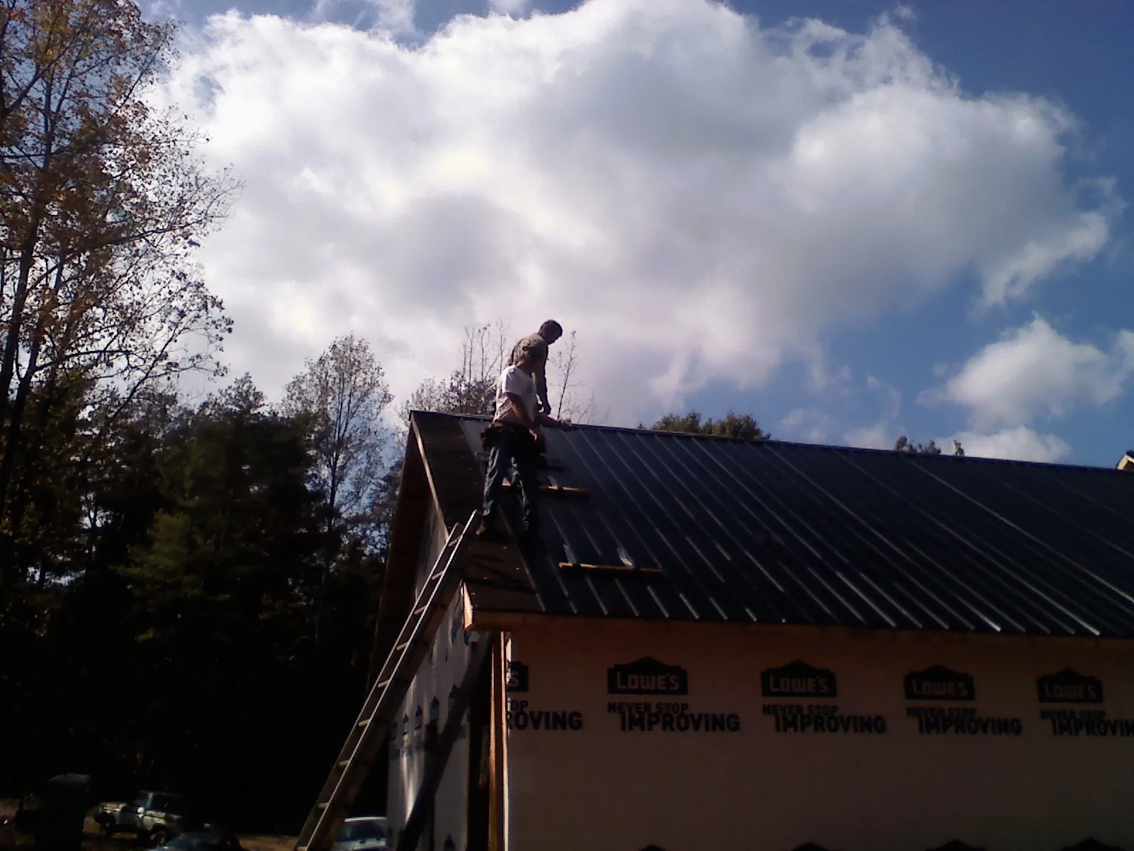 Roofer fastening dark metal panels high against a cloudy sky, from a Roof Inspection job in Gibson Island