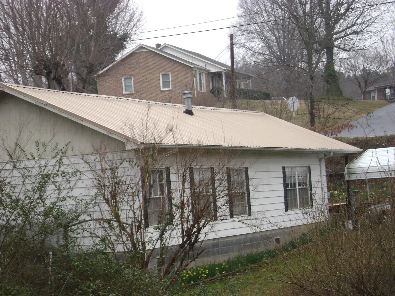 Tan metal roof on a white sided house set into a hillside — Commercial Roofing by Roofing Brothers in Gibson Island